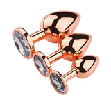 A set of three elegant rose gold jeweled butt plugs with large clear crystals on the base