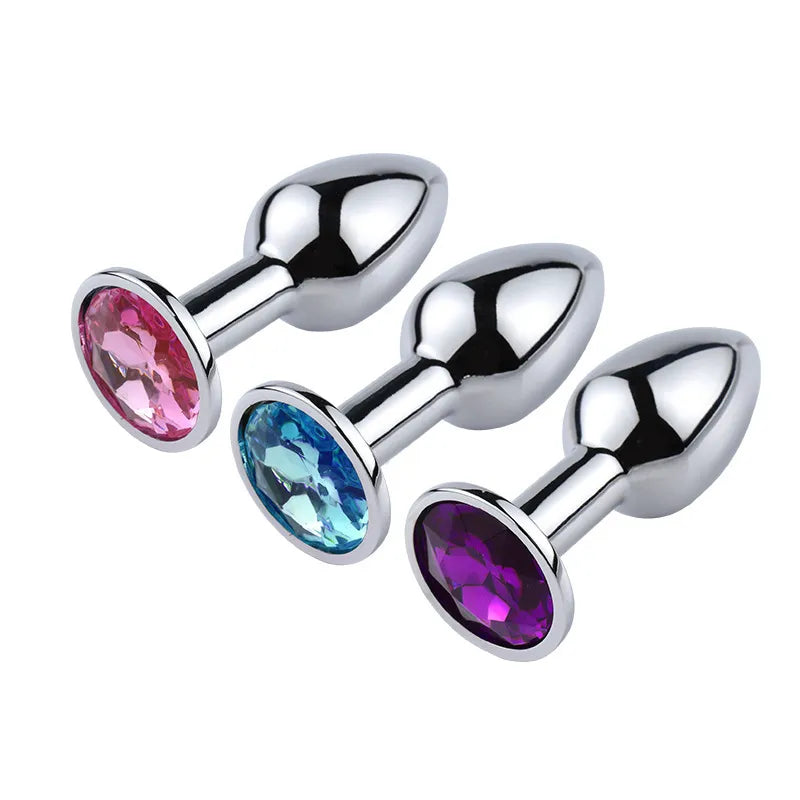 Three silver stainless steel jeweled butt plugs with pink, blue, and purple crystals on the base
